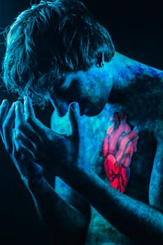 Conceptual portrait of a person with blue body paint and glowing red heart design.